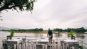 An outdoor dining area with tables and chairs, overlooking a body of water and distant mountains. - Sky Resort (Kanchanaburi)