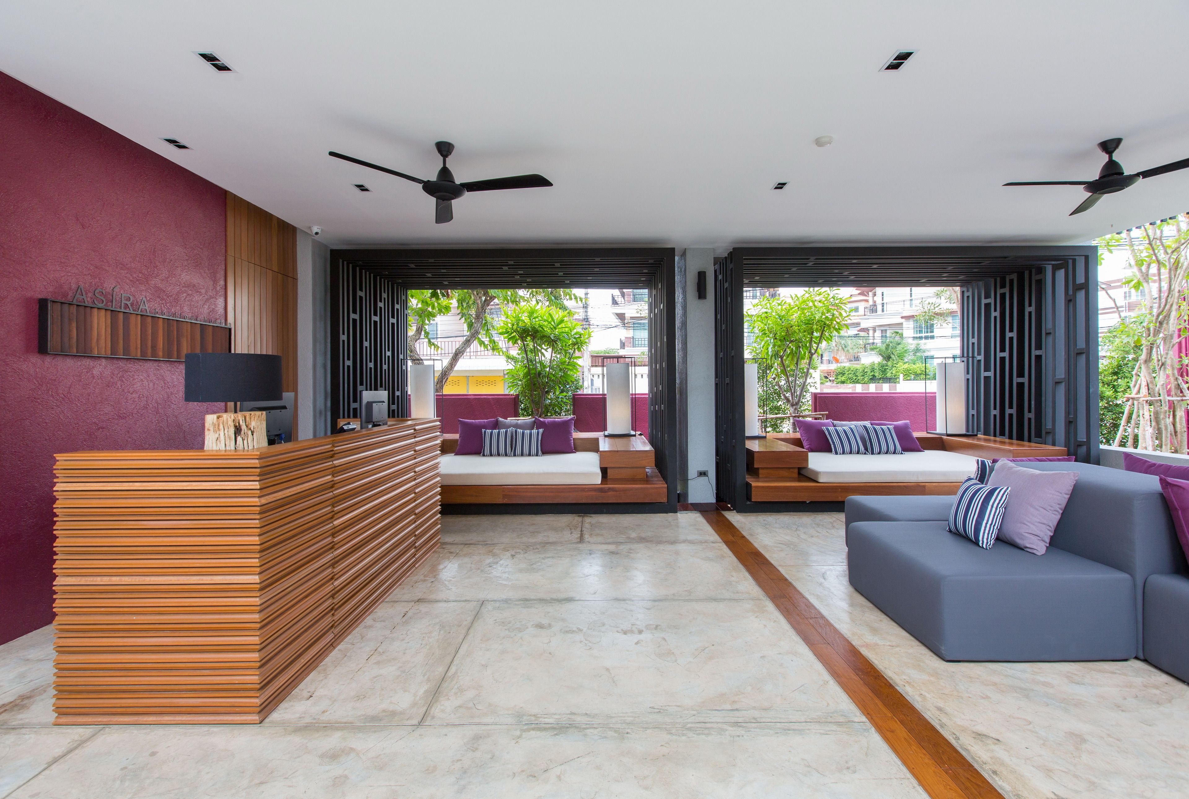 A modern reception area with a wooden reception desk, seating with cushions, and ceiling fans.
