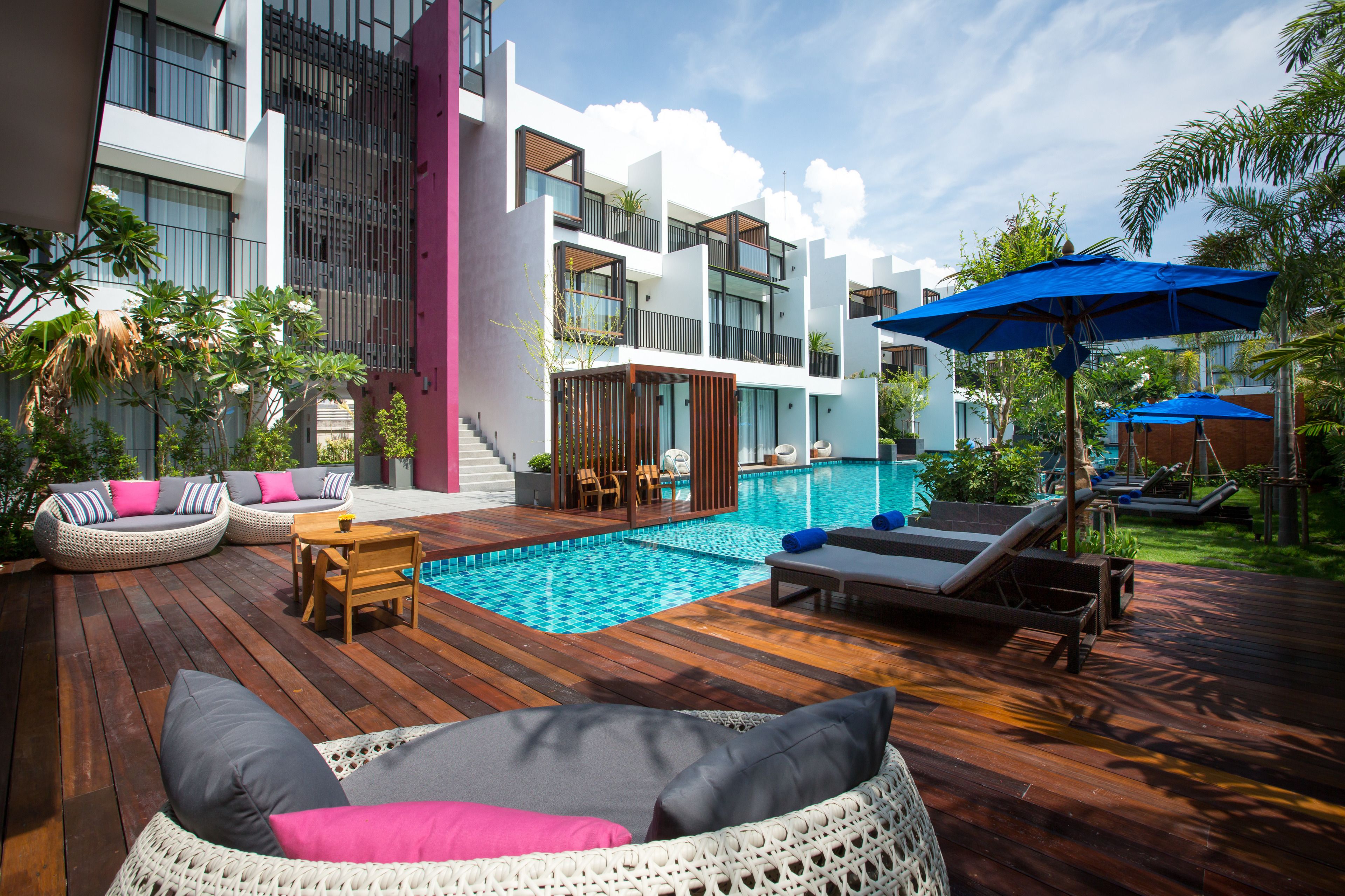 A modern outdoor pool area with wooden decking, lounge chairs, and a small table.