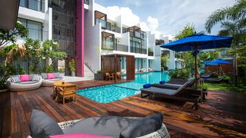 A modern outdoor pool area with wooden decking, lounge chairs, and a small table.