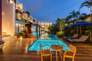 A modern outdoor pool area with a wooden deck, lounge chairs, and a small table. - Asira Boutique HuaHin Hotel (Hua Hin)