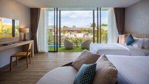 Habitación de hotel con dos camas, un escritorio y un ventanal que ofrece vistas a un patio con plantas y un edificio.