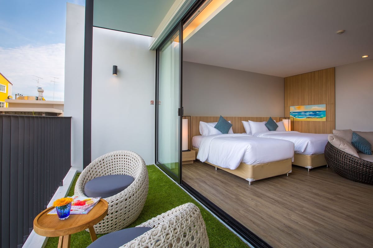 Quarto de hotel moderno com parede de vidro, duas camas, um pequeno espaço de estar e vista para o exterior.