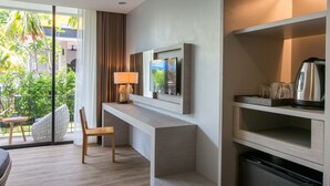 Una habitación de hotel moderna con piso de madera, una zona de estar con una silla y una mesita, un televisor de pantalla plana en la pared y una cafetera en un estante.