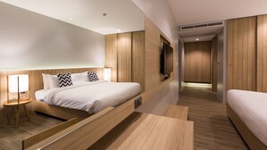 Una habitación de hotel moderna con una cama grande, mesitas de noche, un televisor y un vestidor.
