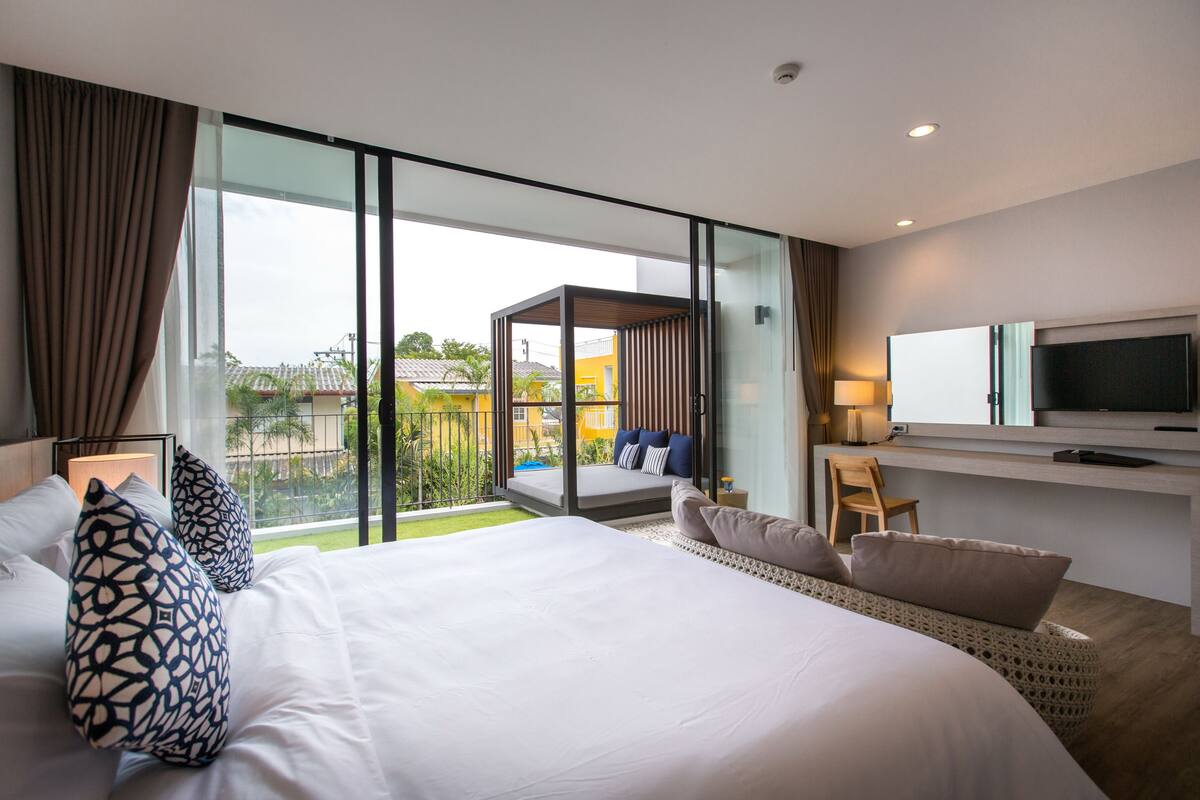 Quarto de hotel moderno com uma cama grande, televisão e varanda com vista para a cidade.
