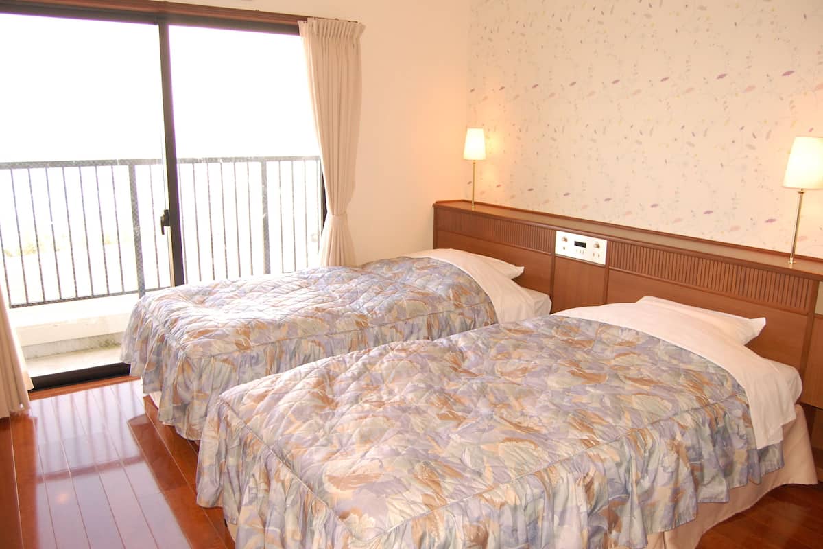A hotel room with two beds, a balcony with a view, and two bedside lamps.