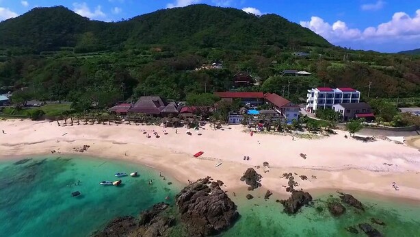 A beach with clear turquoise waters, rocky outcrops, and buildings with red roofs. - Amami Resort Basyayamamura (Amami)