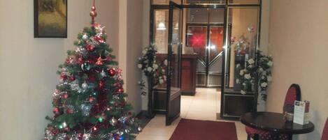 Un vestíbulo de hotel con un árbol de Navidad decorado, una alfombra roja y una escalera que conduce al piso superior.
