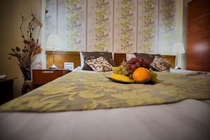 A neatly made bed with a floral bedspread, a fruit plate on the bed, and a nightstand with a lamp and a picture frame.