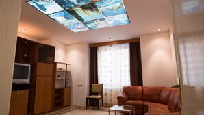 A living room with a brown leather sofa, a glass coffee table, a television on a wooden cabinet, and a ceiling with a stained glass design. - Hotel Rina Cerbul (Sinaia)