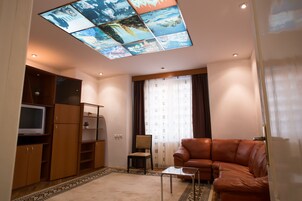 Un salón con un sofá de cuero marrón, una mesa de centro de cristal, un televisor sobre un mueble de madera y un techo con un diseño de vitral.