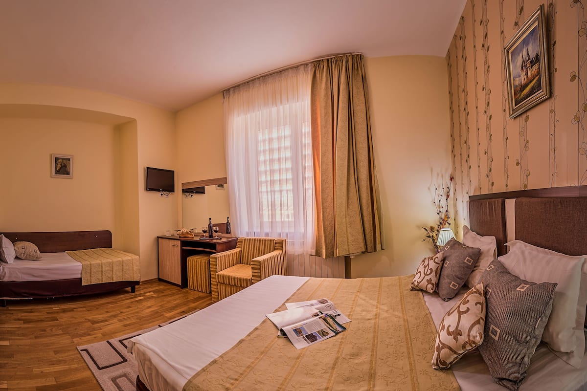 A hotel room with two beds, a desk, a chair, a TV, and a window with curtains.