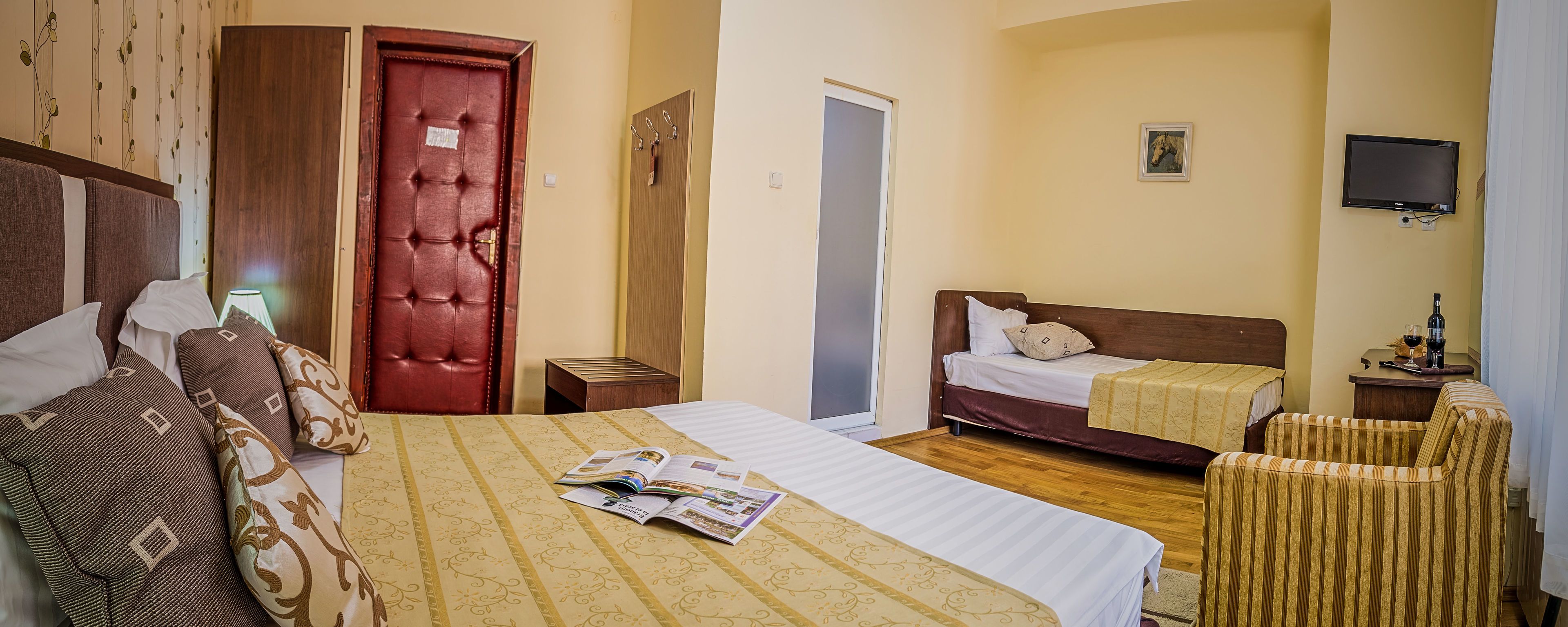 A hotel room with a large bed, a smaller bed, a TV, a wooden door, and a chair.
