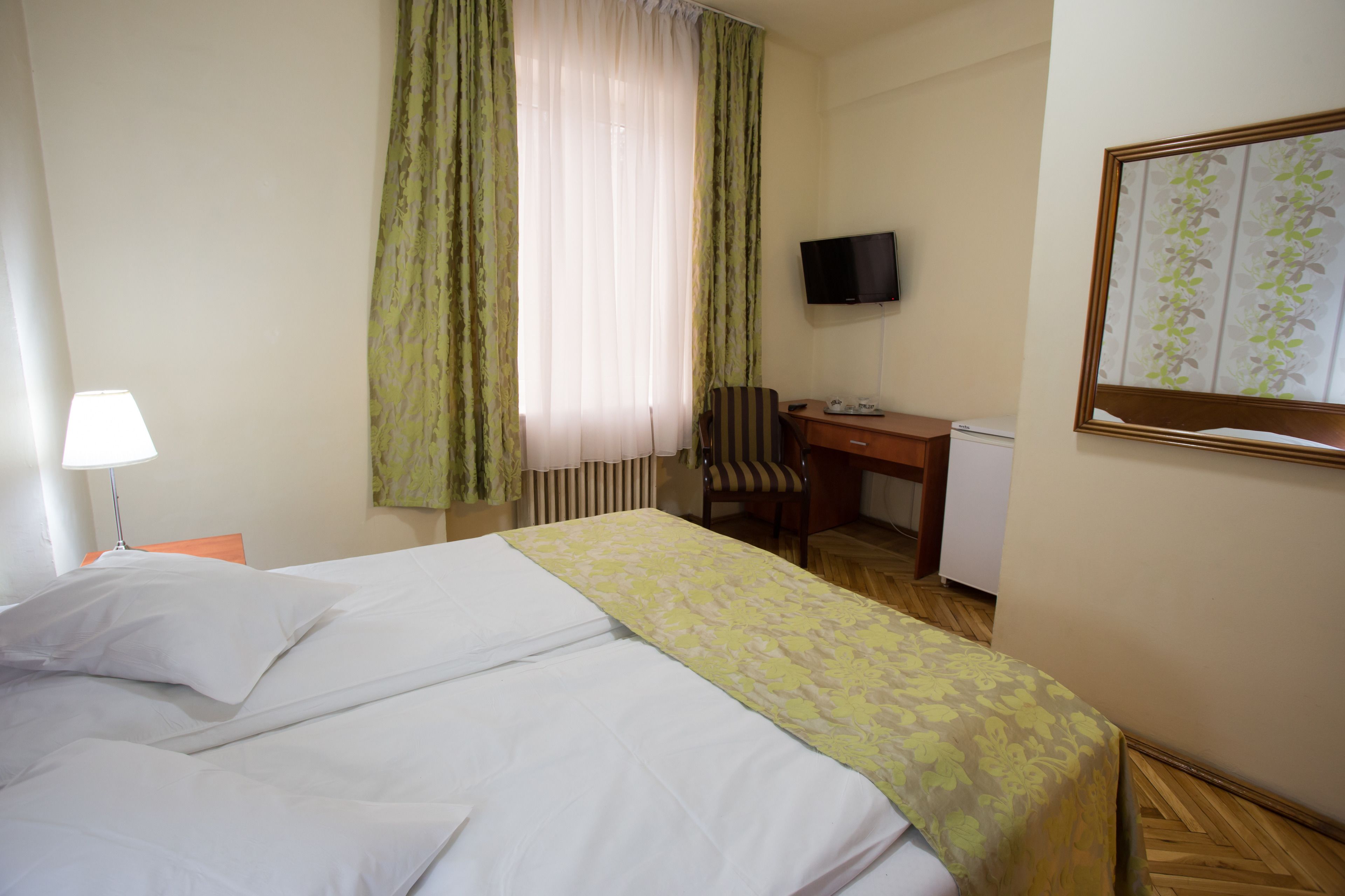 A hotel room with a bed, a desk, a chair, a television, and a window with curtains.