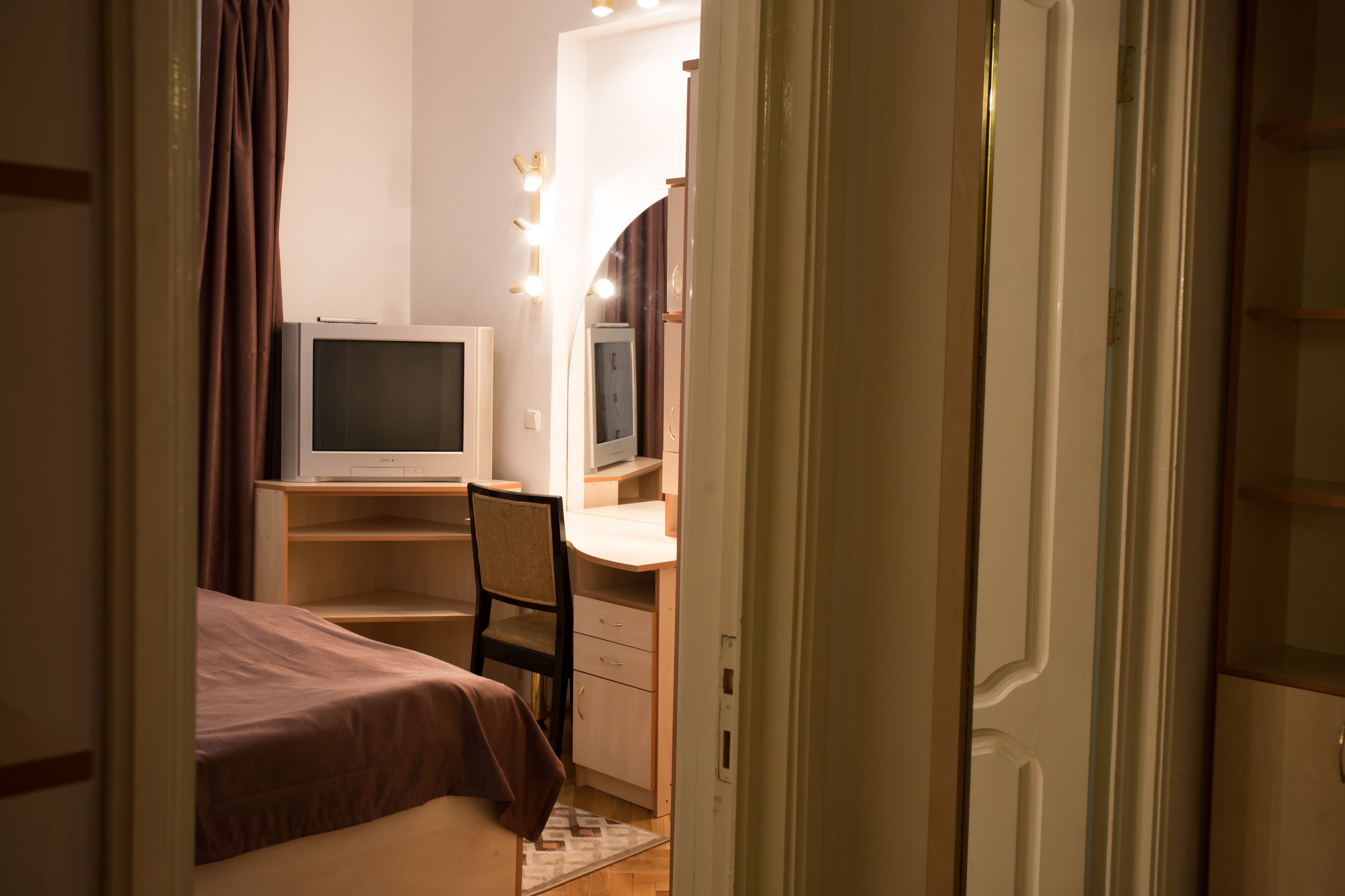 A bedroom with a bed, a desk with a computer, a chair, and a mirror with lights.