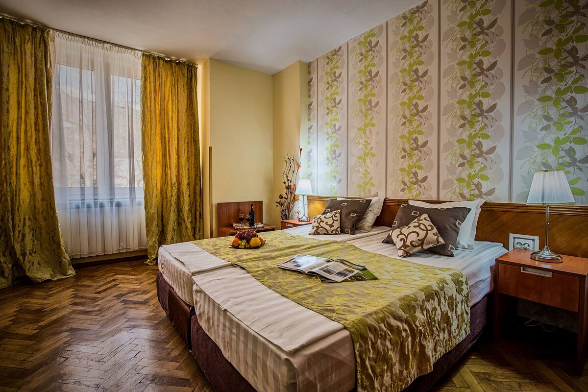 A hotel room with a large bed, a nightstand, a lamp, and a window with curtains.