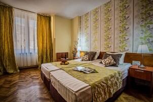 Una habitación de hotel con una cama grande, una mesita de noche, una lámpara y una ventana con cortinas.