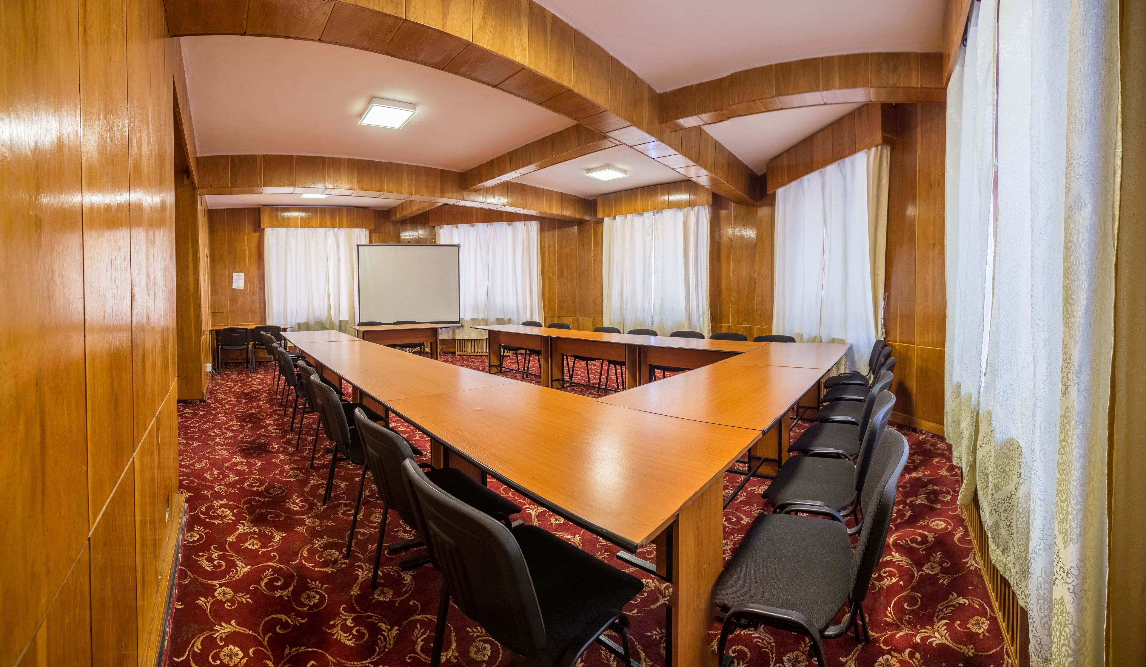 Ein Konferenzraum mit einem langen Tisch, Stühlen, einer Tafel und Vorhängen.