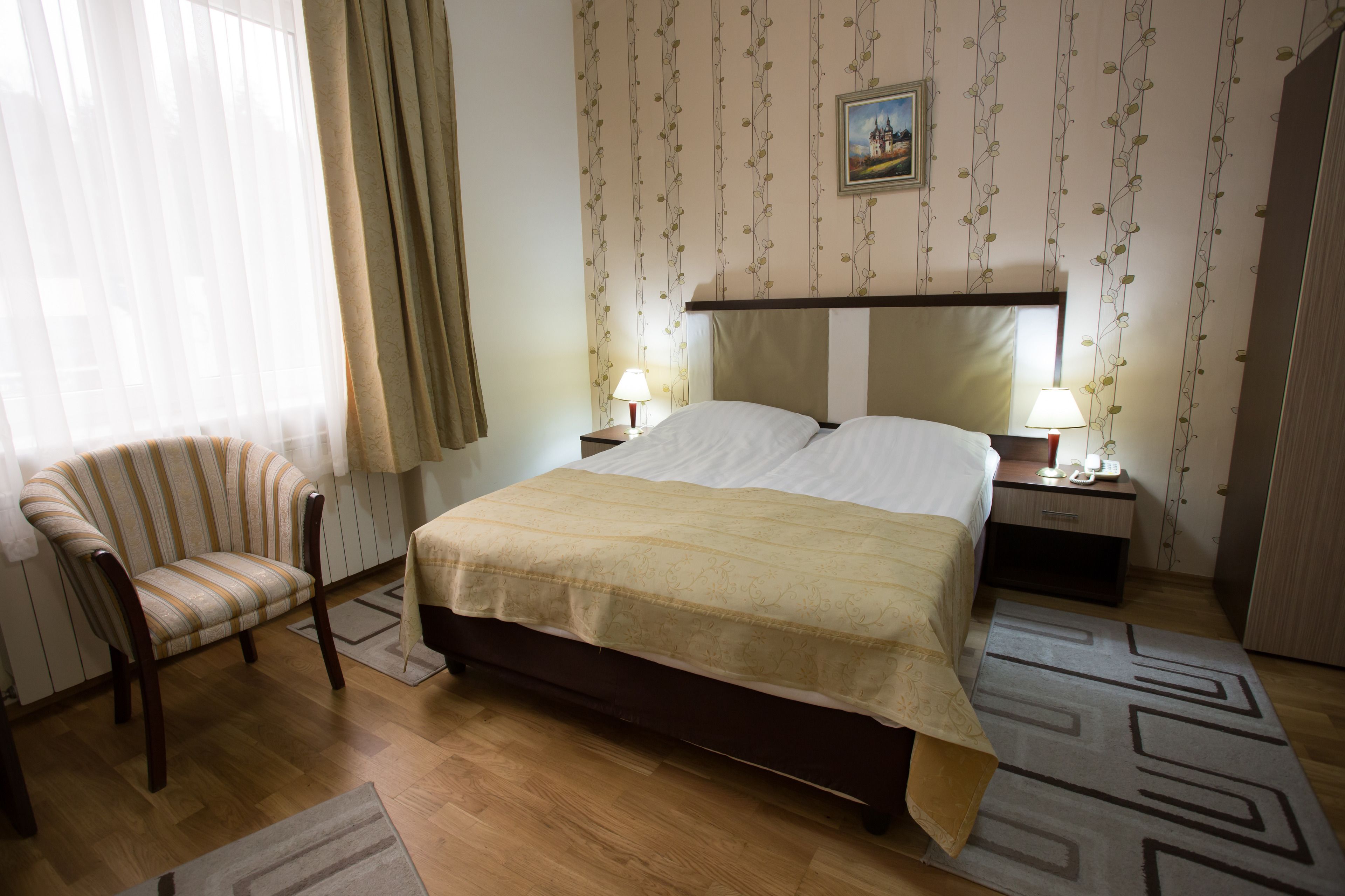 Une chambre d’hôtel avec un lit, une chaise, deux tables de chevet avec des lampes, un tableau au mur et un tapis à motifs.
