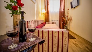 A room with a bed, a table with a bottle and glasses, and a vase with red roses. - Hotel Rina Cerbul (Sinaia)