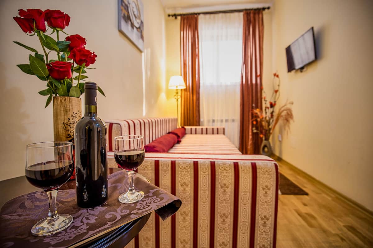 A room with a bed, a table with a bottle and glasses, and a vase with red roses.