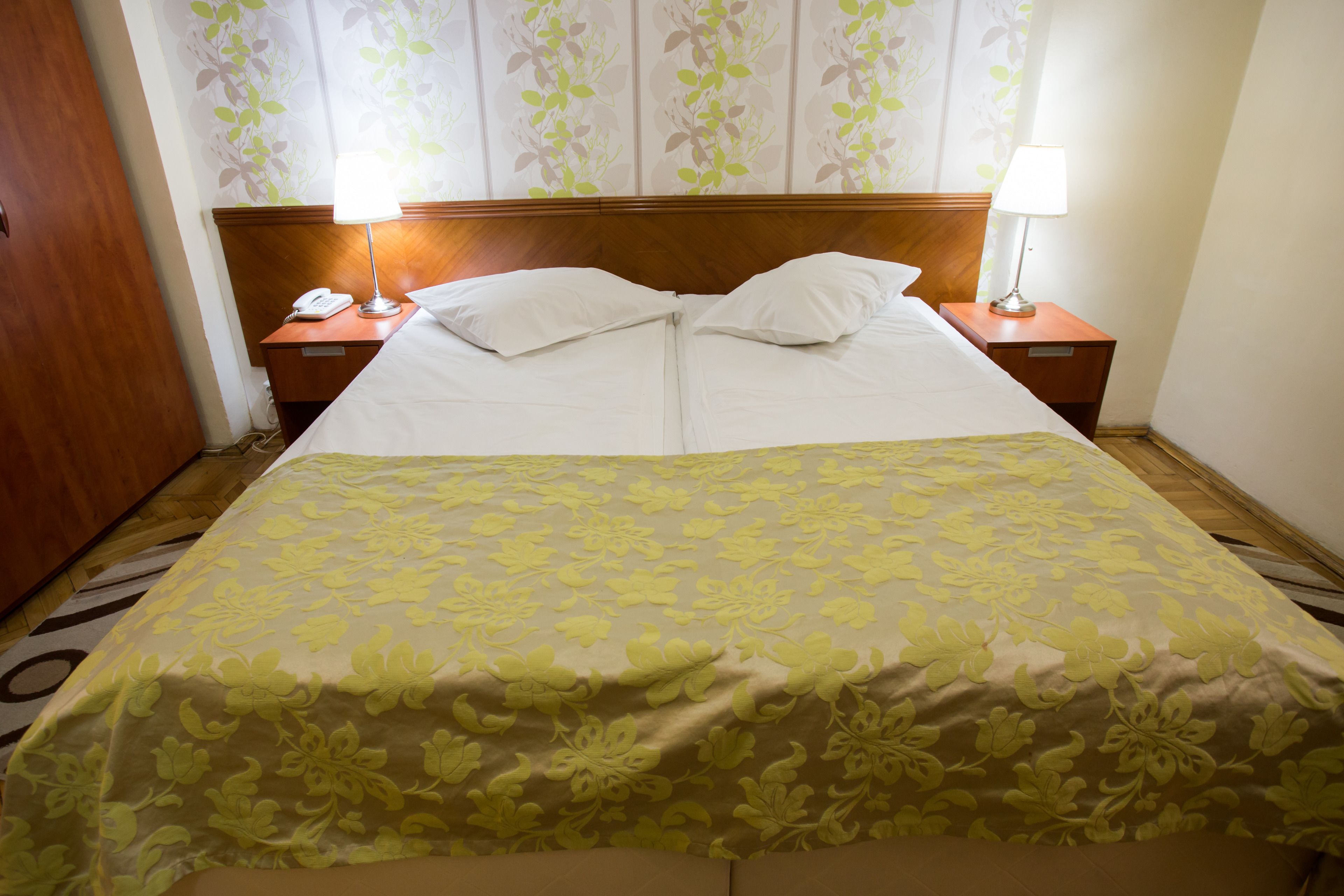A hotel room with a bed, two bedside tables, a telephone, and a lamp on each table.