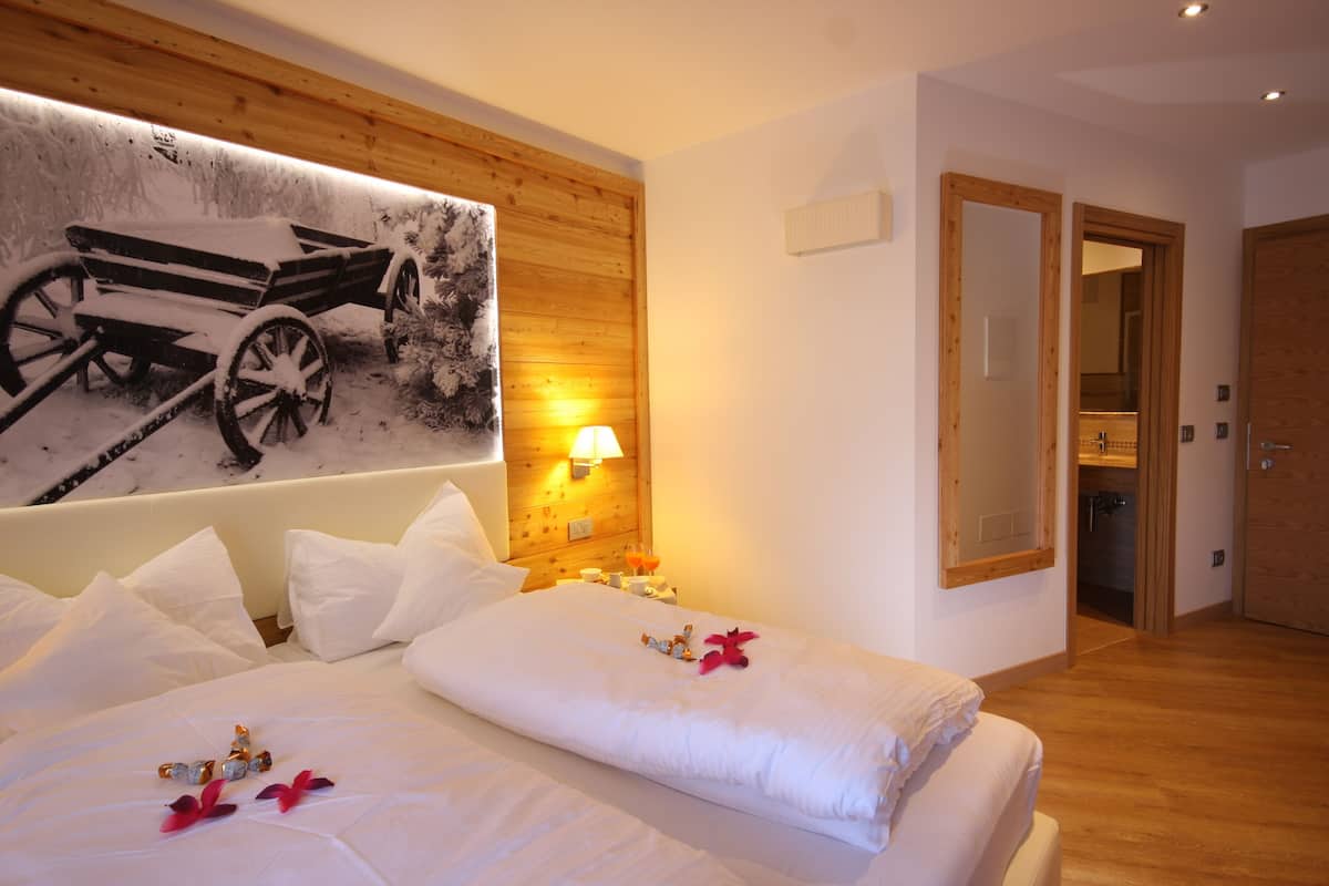 Ein Hotelzimmer mit einem Bett, weißer Bettwäsche, einer Wandlampe, einem Holz-Kopfteil und einer Tür zu einem Badezimmer.