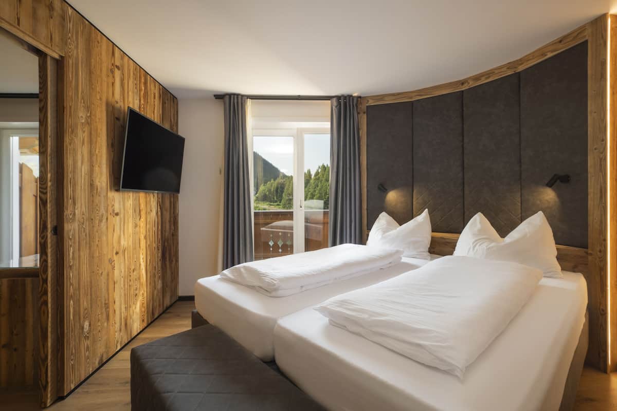 Ein modernes Hotelzimmer mit einer Wand in Holzoptik, einem Flachbildfernseher, zwei Betten mit weißer Bettwäsche und Blick ins Freie.
