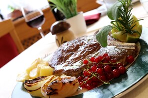 A plate with a steak, roasted potatoes, grilled onions, red currants, and a sprig of rosemary.