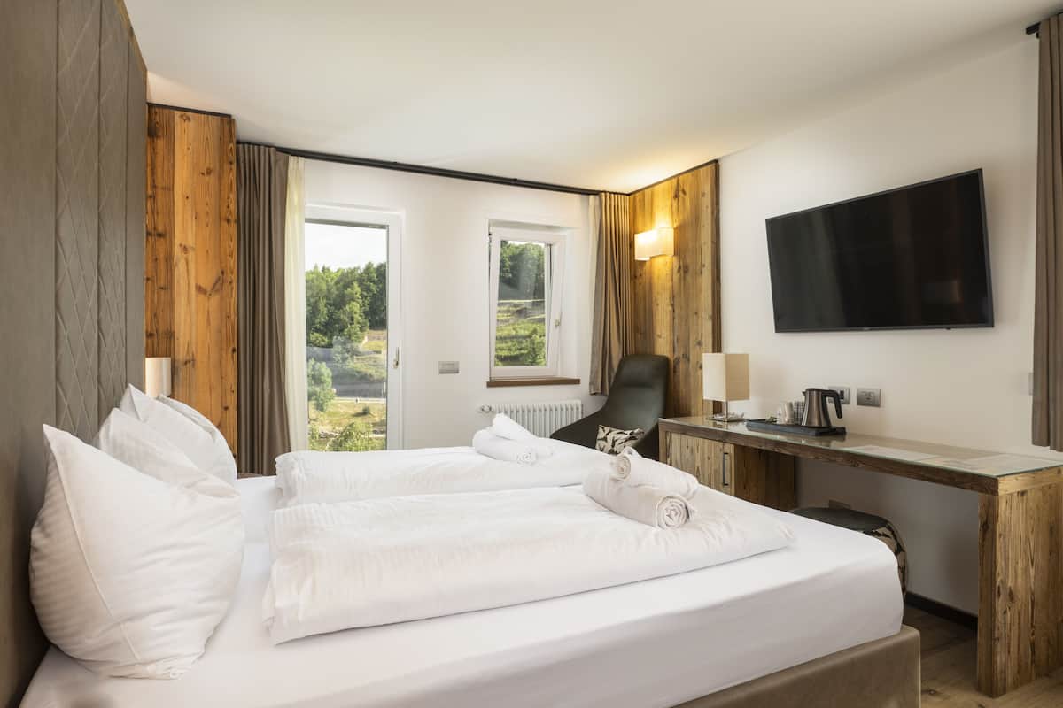 Ein Hotelzimmer mit Bett, Schreibtisch, Stuhl, Fernseher und Blick auf Grünflächen.