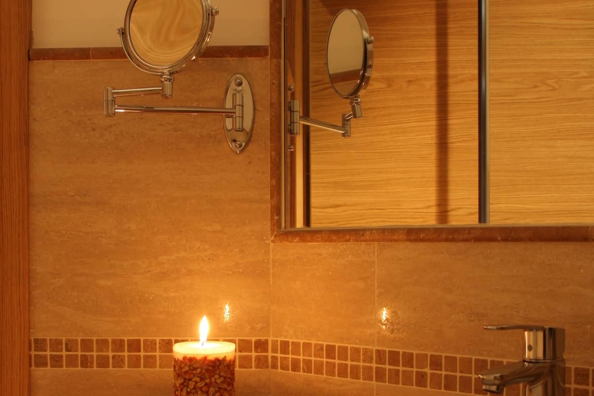 Ein Badezimmer mit einem Holzkosmetikschrank, einem Spiegel, einer brennenden Kerze und einem Handtuch auf der Ablagefläche.