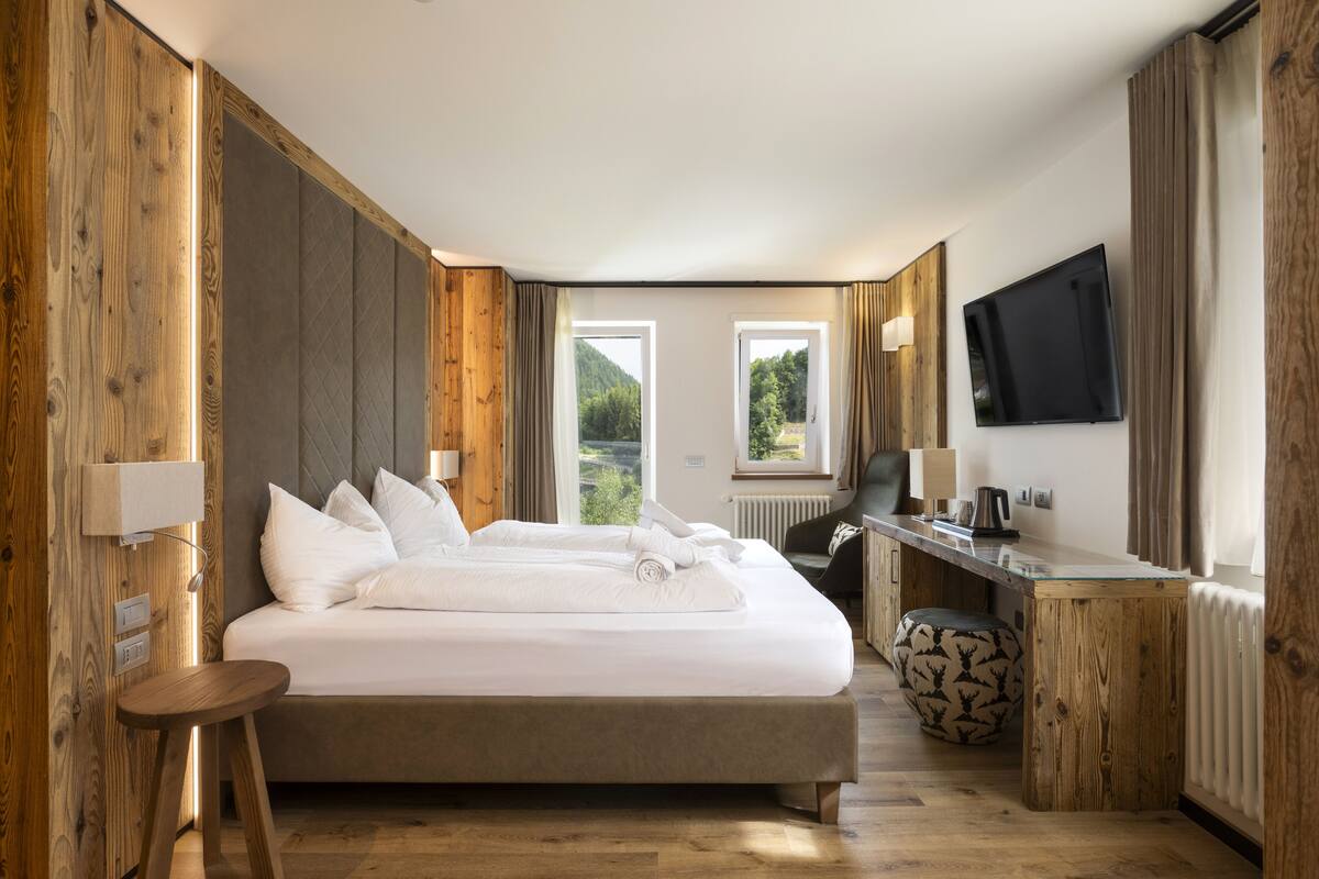 Ein modernes Hotelzimmer mit einem großen Bett, einem Schreibtisch, einem Sessel, einem Fernseher und Blick ins Freie.