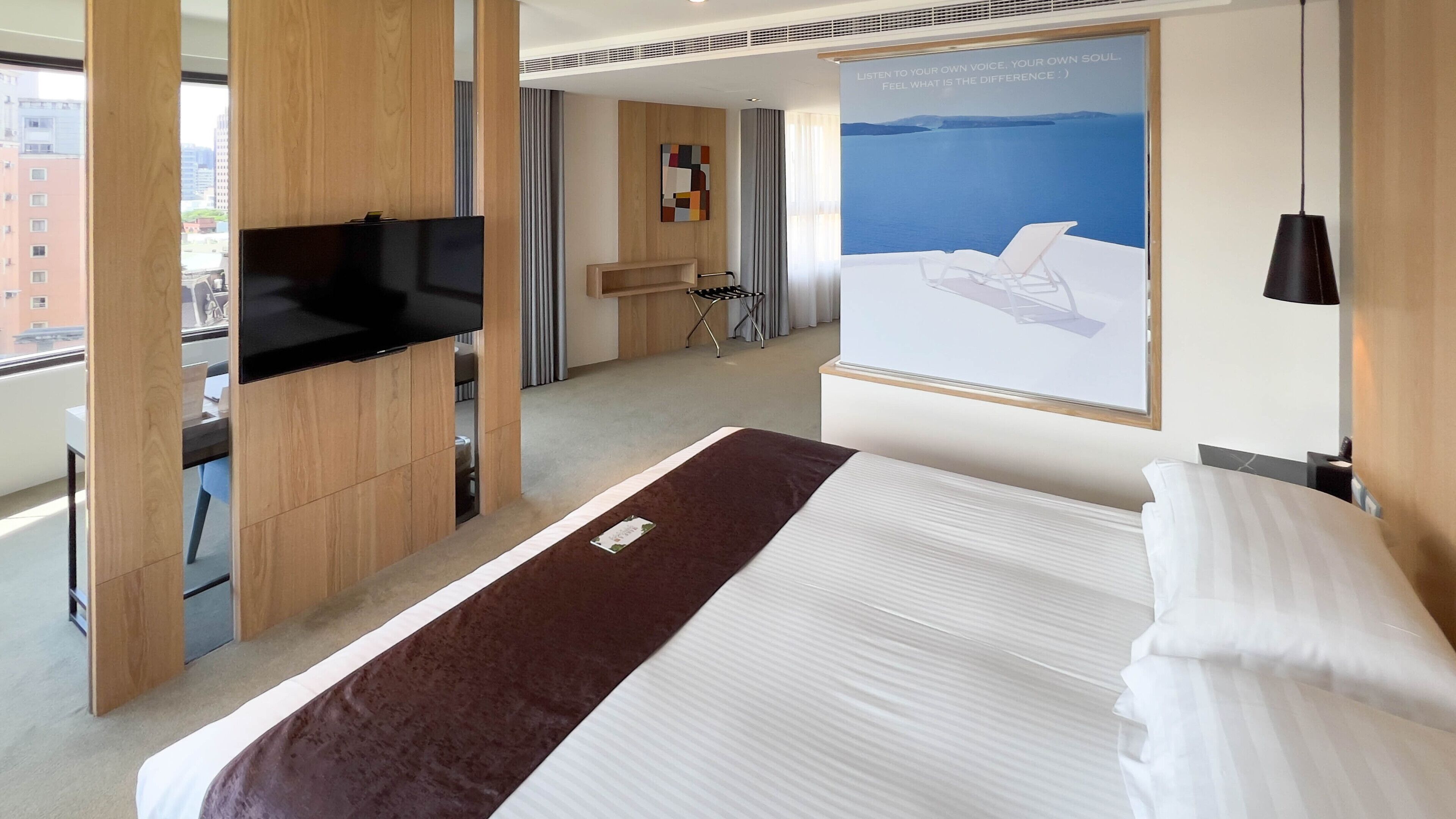 Een hotelkamer met een bed, een televisie, een bureau en een poster van een strand.