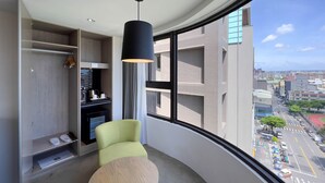 A modern room with a curved window, a green chair, a small table, and a black pendant light. - GOGO HOTEL 38 (Taichung)