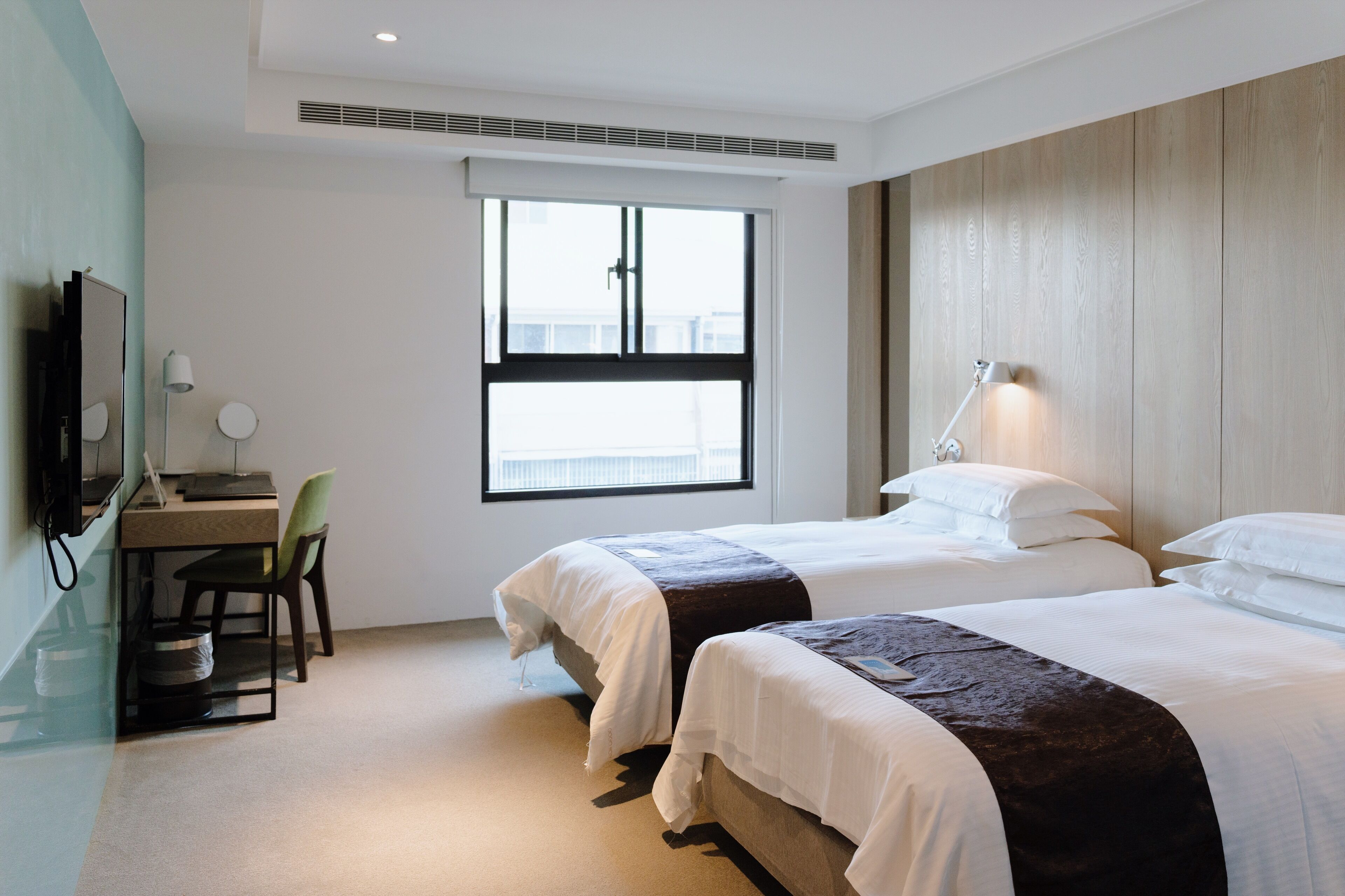 A hotel room with two beds, a desk with a chair, a television, and a window with a view.