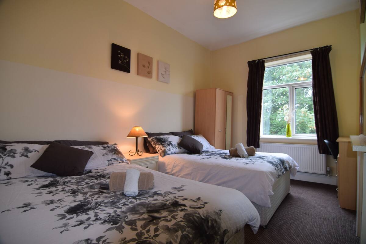 A hotel room with two beds, a window with curtains, a lamp, and a cabinet.