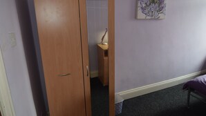 A room with a wooden wardrobe, a bedside table with a lamp, and a purple bed. - Manu's Guesthouse (Birmingham)
