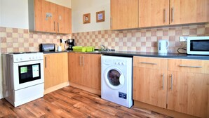 A kitchen with wooden cabinets, a washing machine, a stove, and a microwave. - Manu's Guesthouse (Birmingham)