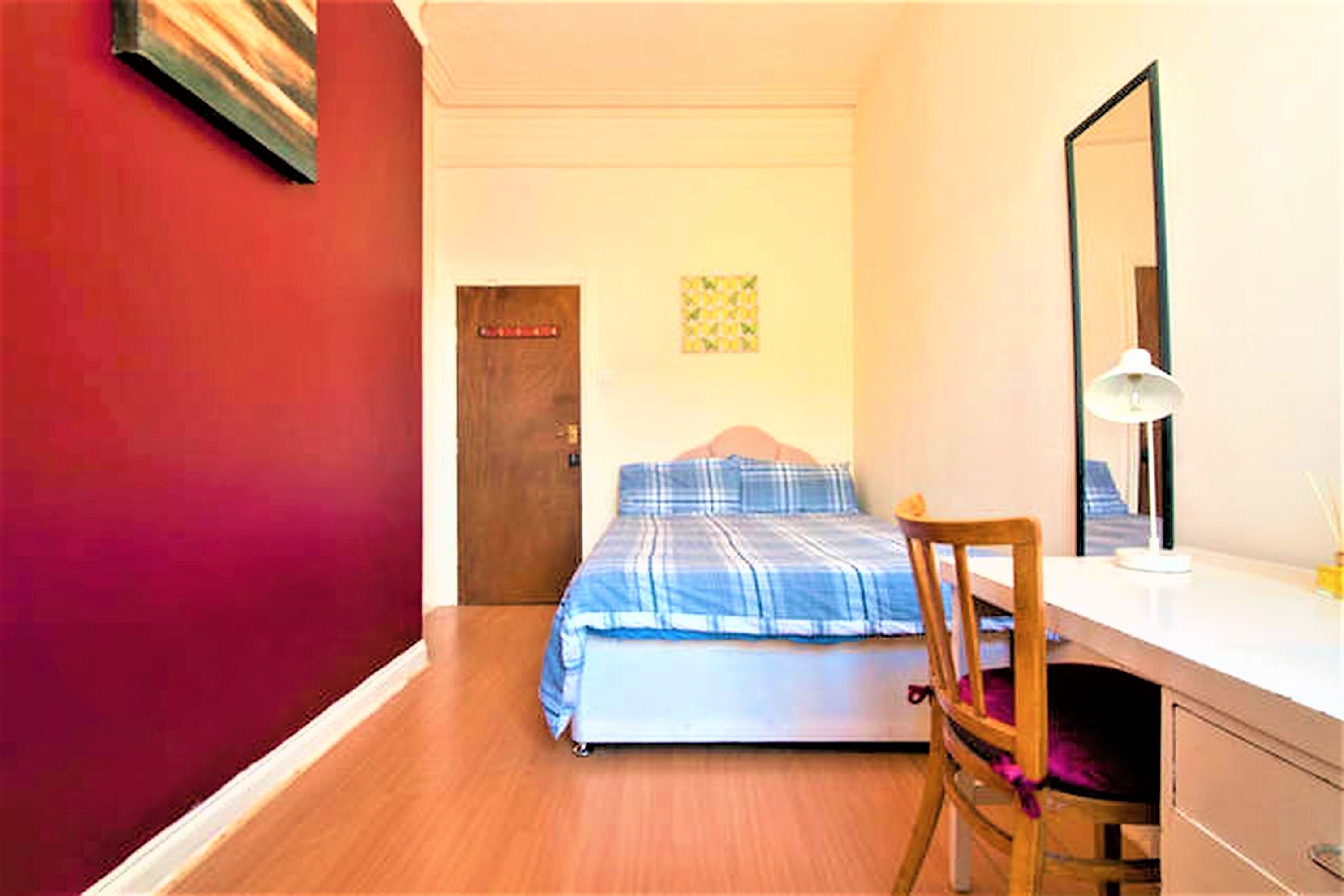 A bedroom with a bed, a desk, a chair, a door, and a wall with a picture.