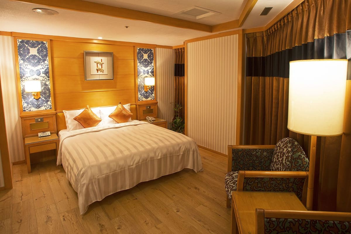 Une chambre d’hôtel avec un grand lit, deux tables de chevet avec des lampes, une chaise et un téléviseur fixé au mur.
