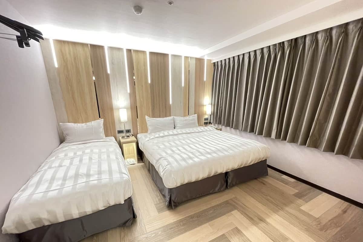 Une chambre d’hôtel avec deux lits, un canapé, un plancher en bois et des rideaux.