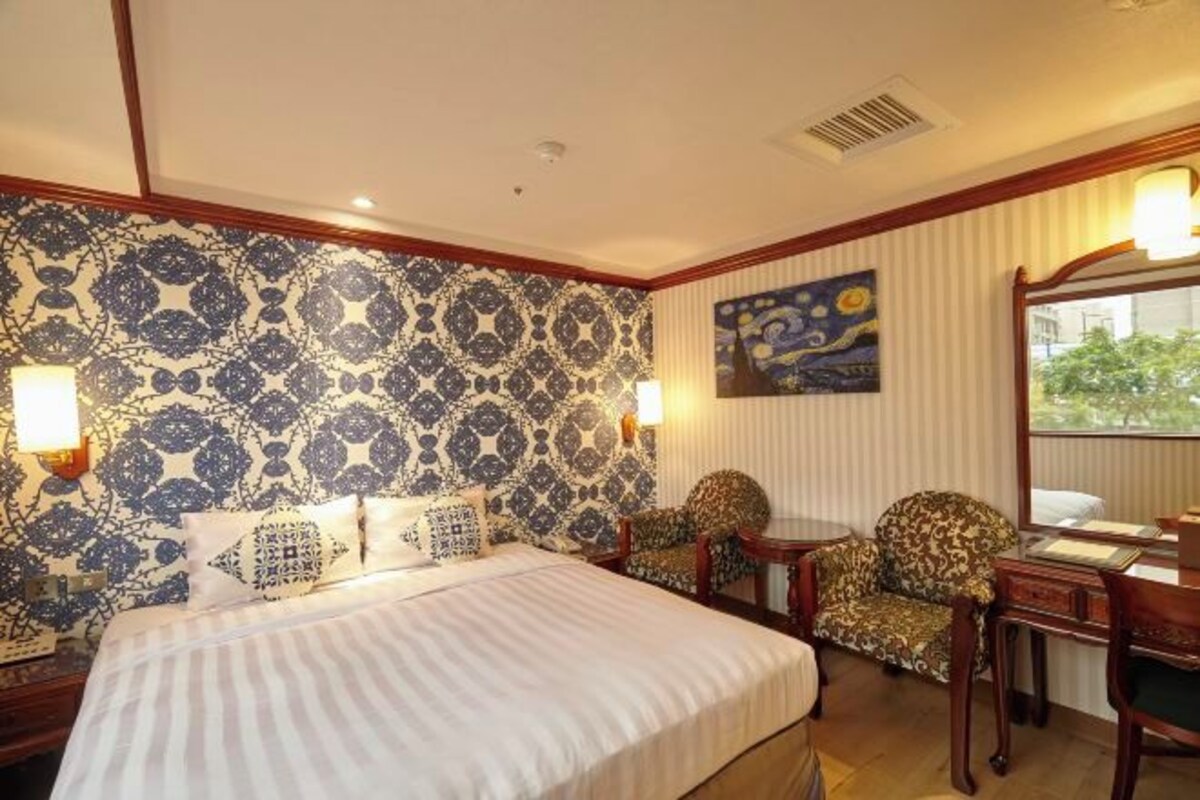 Habitación de hotel con una cama grande, papel tapiz estampado, un cuadro y vistas al exterior.