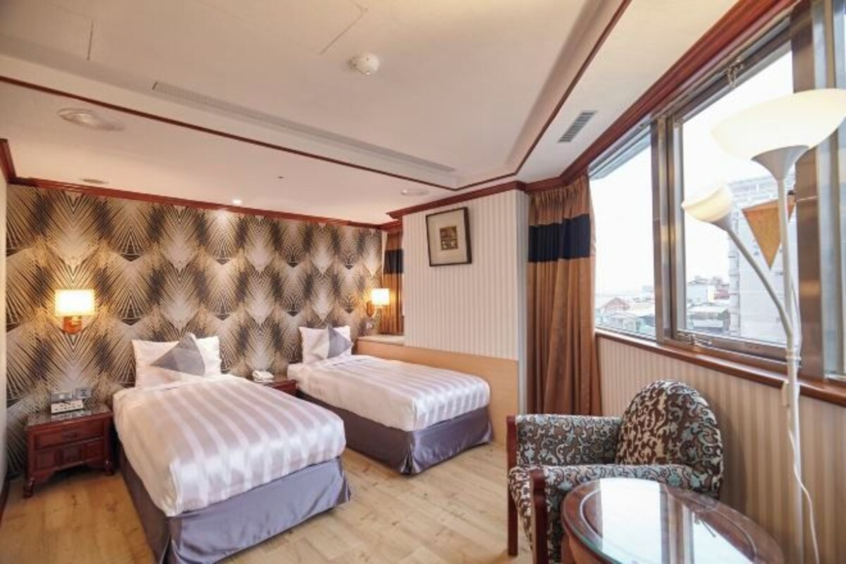 Una habitación de hotel con dos camas, un sofá, una mesa y un ventanal con cortinas.