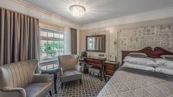 A hotel room with a bed, a desk, a chair, a window with curtains, and a patterned wall.