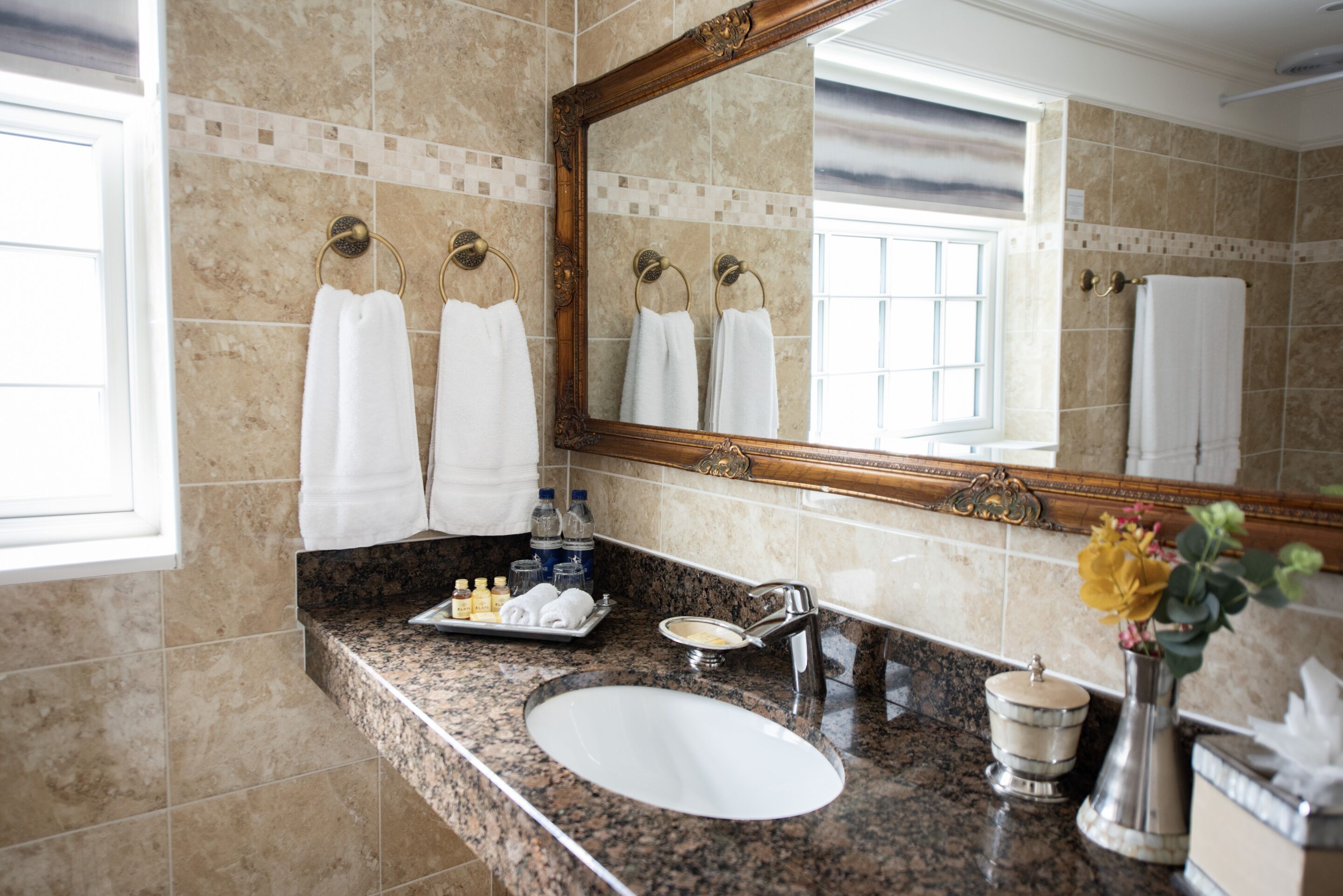 A bathroom with a marble sink, a large mirror, and multiple white towels hanging on towel rings.
