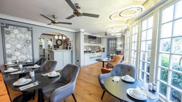 Spiseplads med et moderne køkken i baggrunden, store vinduer og en loftsvift.
