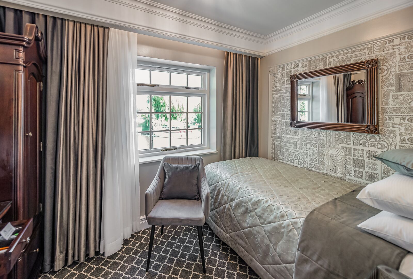 A hotel room with a bed, a chair, a window, and a mirror.