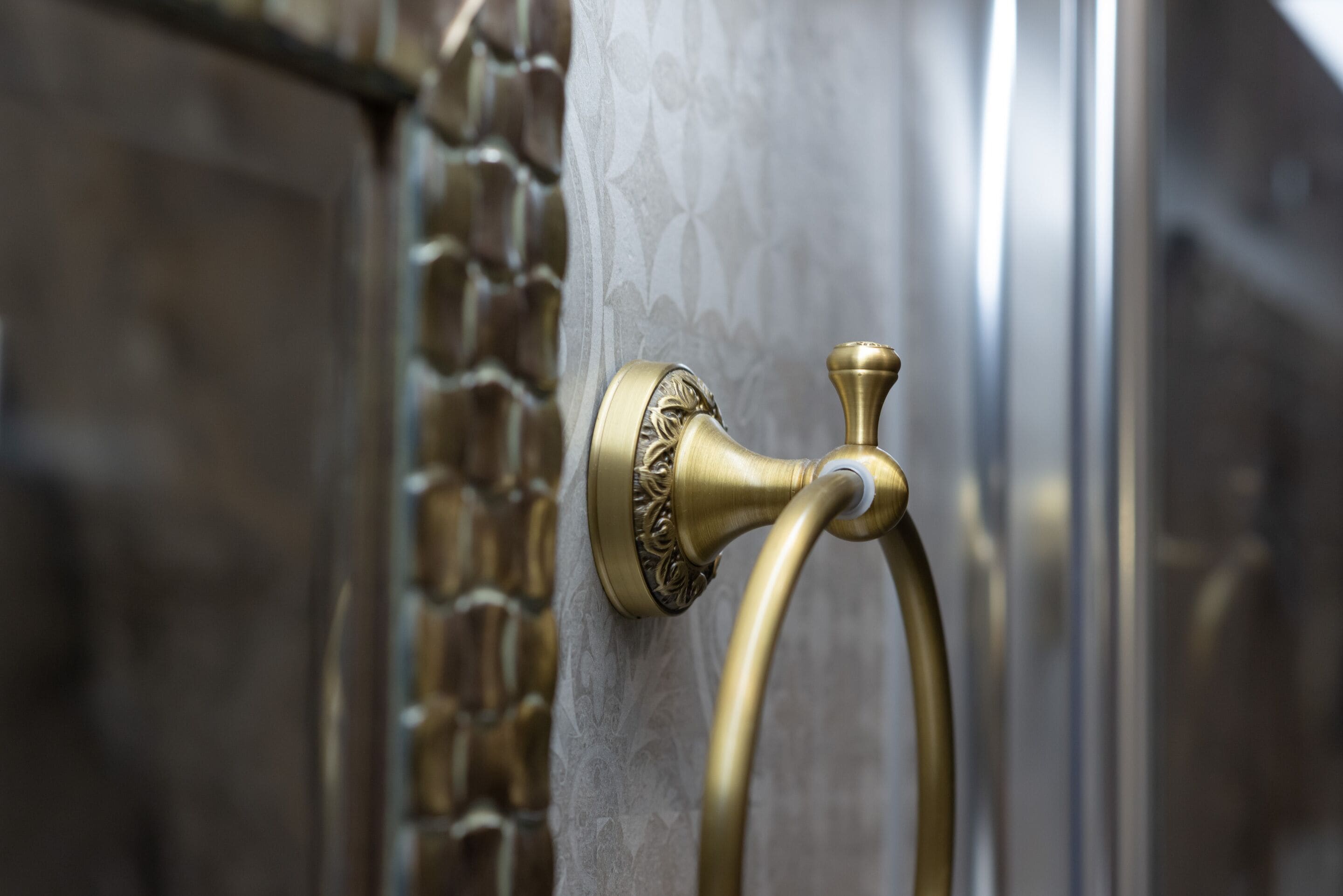 A brass door handle with a decorative design, mounted on a textured wall.