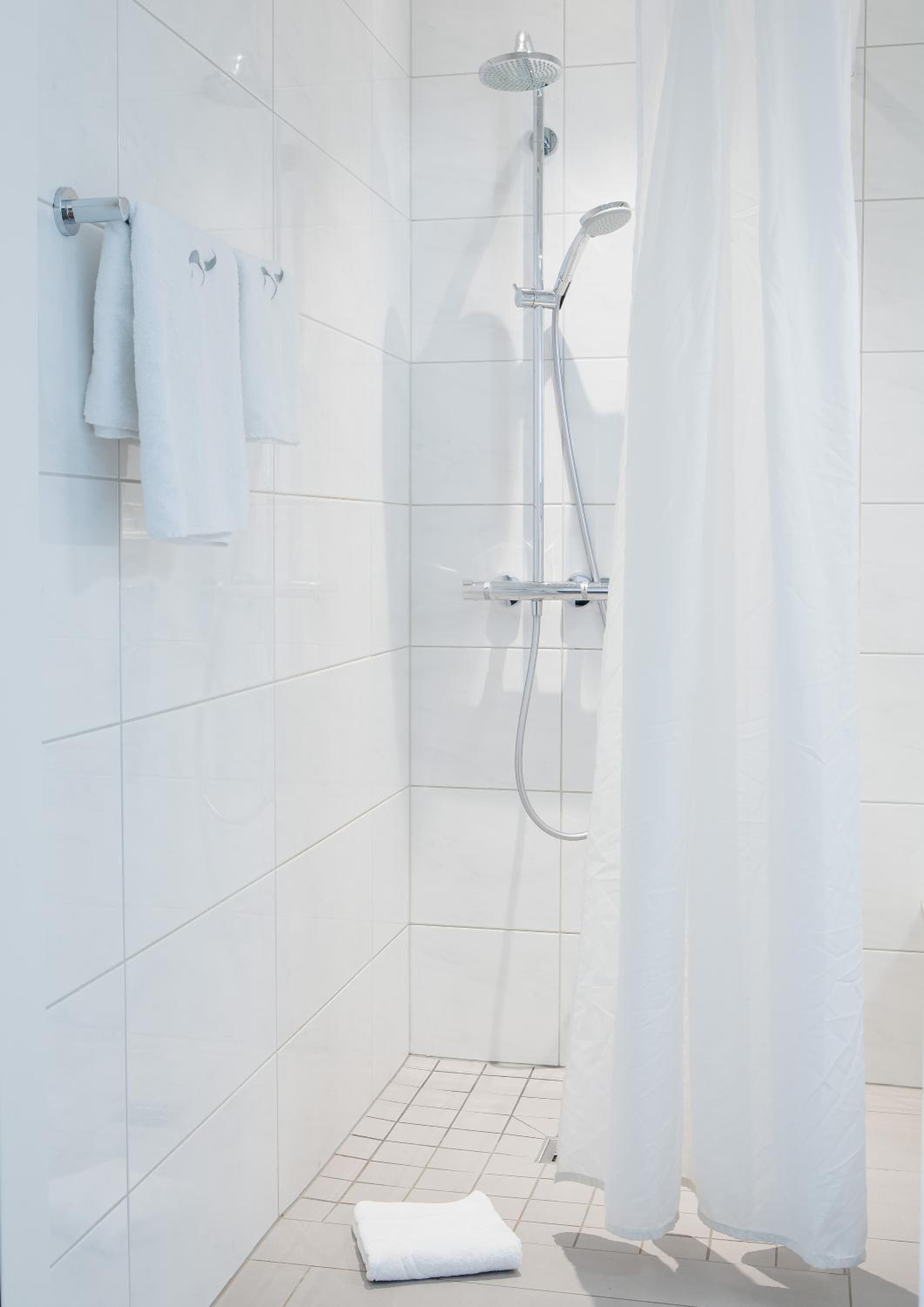 A modern shower area with a glass door, a handheld showerhead, and a wall-mounted towel rack with towels.